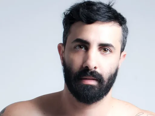 Man met volle donkere baard en kort donker haar op een lichtblauwe achtergrond.