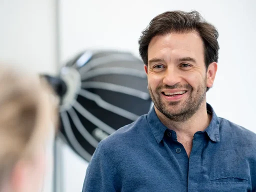 Glimlachende man met donker haar en stoppelbaard in een blauw overhemd.