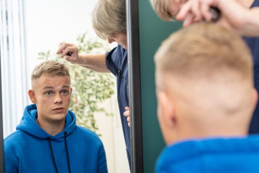Dennis Schouten kijkt in de spiegel terwijl een specialist zijn haargroei controleert na een haartransplantatie.