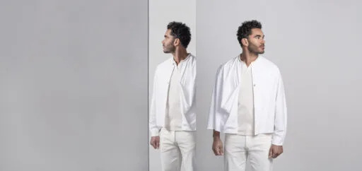 Man met volle krullen in witte kleding kijkt in een spiegel, symbool voor het plannen van een haartransplantatieconsult.