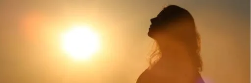 Silhouet van een vrouw met lang haar die baadt in zonlicht als symbool voor vitamine D en haargroei na haartransplantatie.