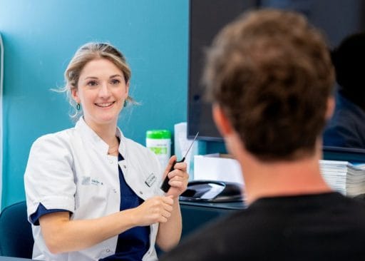 Vrolijke vrouwelijke arts legt iets uit aan een patiënt tijdens een consult over haartransplantatie, glimlachend in witte jas.