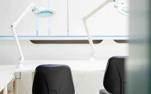 Twee zwarte stoelen aan een witte werkbank met verlichte loeplampen in een haartransplantatiekliniek.