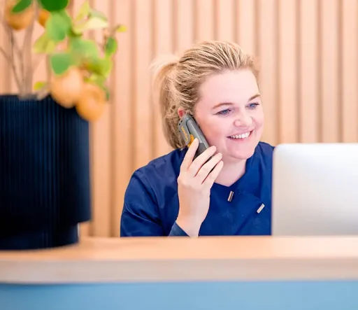 Vriendelijke receptioniste aan de telefoon bij de balie van een haartransplantatiekliniek.