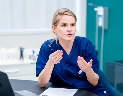 Vrouwelijke arts in blauwe scrubs gebaart en legt een haartransplantatieprocedure uit tijdens een consult.