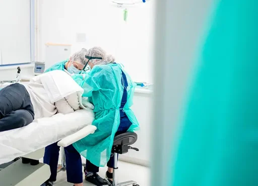 Chirurgen in groene operatiekleding gebogen over een liggende patiënt tijdens een haartransplantatie.