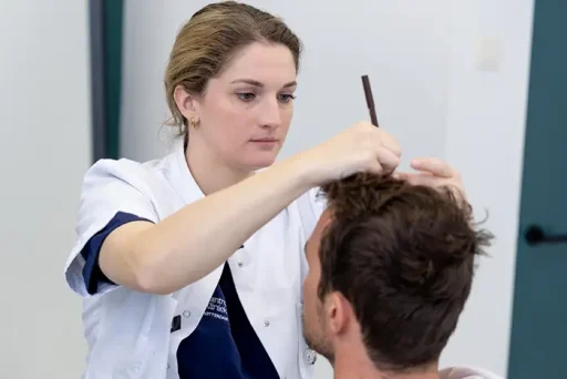Zorgprofessional onderzoekt het haar van een man met een kam tijdens een nazorgconsult na een haartransplantatie.
