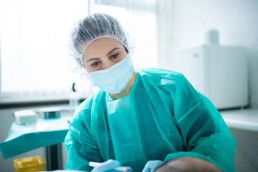 Chirurg in groene operatiekleding met haarnetje en mondmasker concentreert zich op een haartransplantatieprocedure.