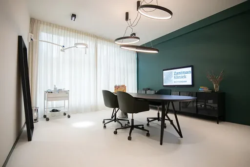 Moderne spreekkamer van de Zantman Kliniek met een ronde tafel, stoelen en presentatiescherm voor een haartransplantatieconsult.