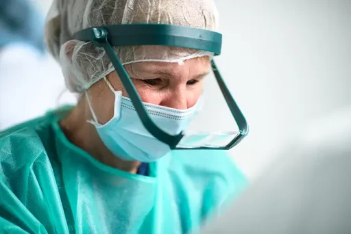 Chirurg in groene operatiekleding kijkt geconcentreerd naar haartransplantatie met loepbril.