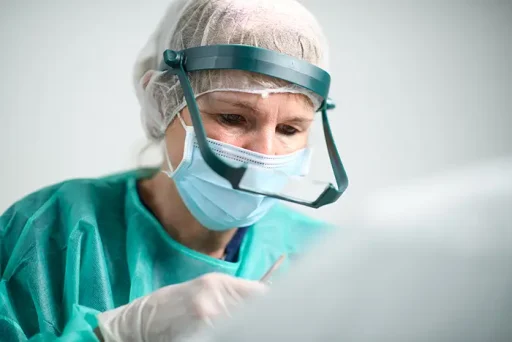 Chirurg in groene operatiekleding en loepbril voert nauwkeurig een haartransplantatie uit.