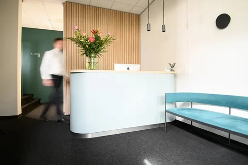 Moderne wachtruimte van haartransplantatiekliniek met lichtblauwe balie en bankje, persoon loopt voorbij.