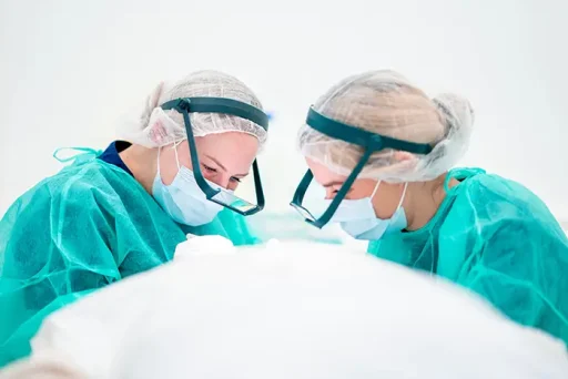 Twee chirurgen in groene scrubs en steriele bescherming buigen zich over een patiënt tijdens een haartransplantatie.