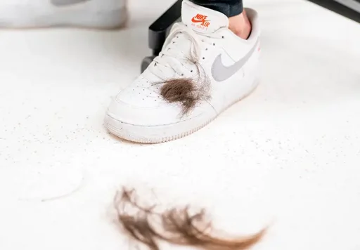 Witte Nike-sneaker met afgeschoren haar op en rond de schoen, symbool voor voorbereidend scheren bij een haartransplantatie.