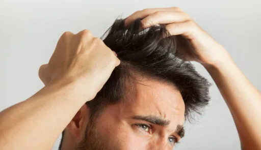 Man met beginnende haaruitval bekijkt zijn terugtrekkende haarlijn met zorg, een teken van kaal worden en haarverlies.
