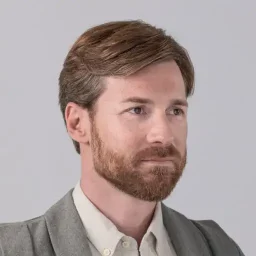 Portret van een man met een natuurlijke haarlijn en dik, gezond haar na een haartransplantatie bij Zantman Kliniek, op een grijze achtergrond.