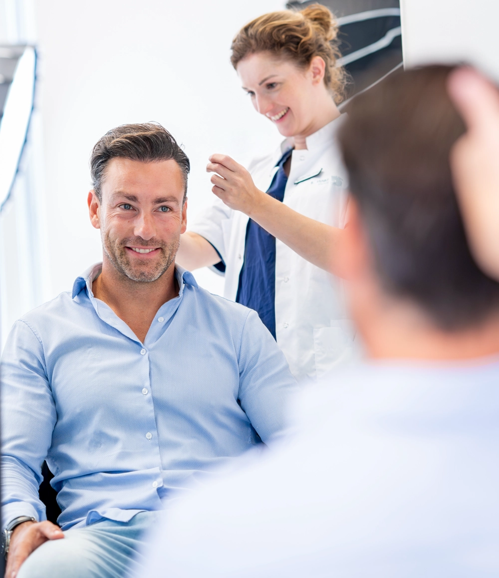 Man zit in stoel terwijl een arts achter hem uitleg geeft tijdens een haartransplantatie consult